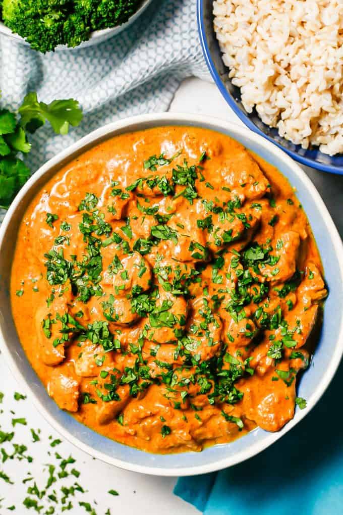 Butter chicken in a blue and white bowl topped with fresh parsley with a bowl of rice nearby.