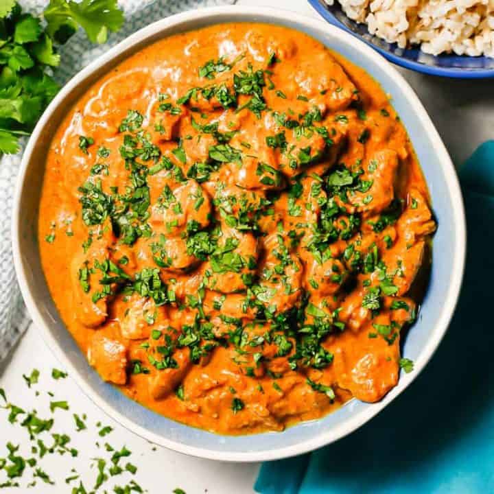 Crock pot butter chicken served in a large bowl with parsley on top and parsley sprigs to the side.