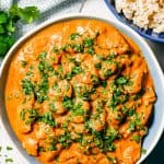 Butter chicken in a blue and white bowl topped with fresh parsley with a bowl of rice nearby and a text overlay on the photo.