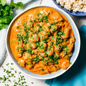 Close up of saucy butter chicken in a blue and white bowl with parsley on top and to the side.