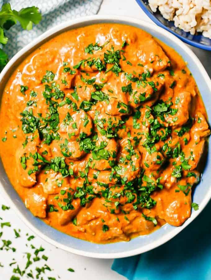 Close up of saucy butter chicken in a blue and white bowl with parsley on top and to the side.