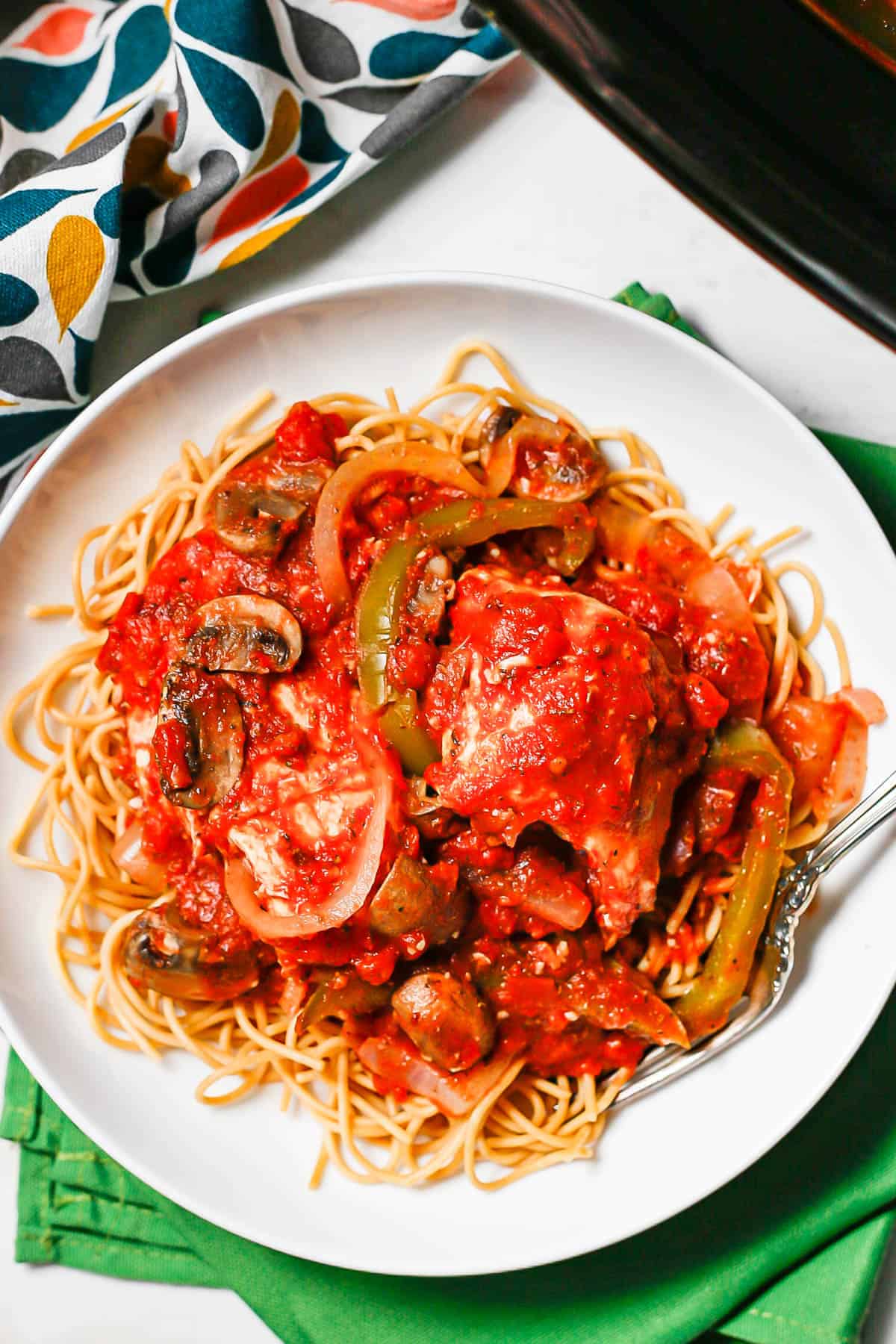 A low white bowl set on green napkins and filled with spaghetti topped with chicken cacciatore.