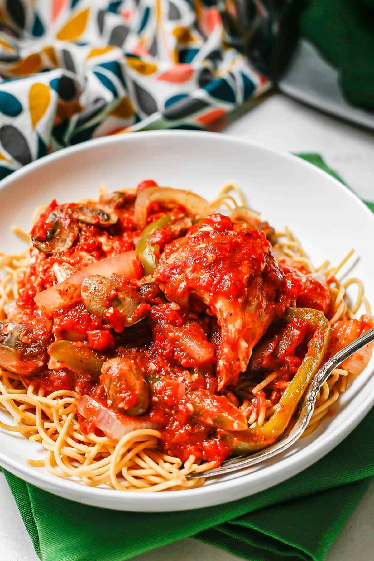 Chicken cacciatore served over spaghetti in a low white bowl with a fork to the side.