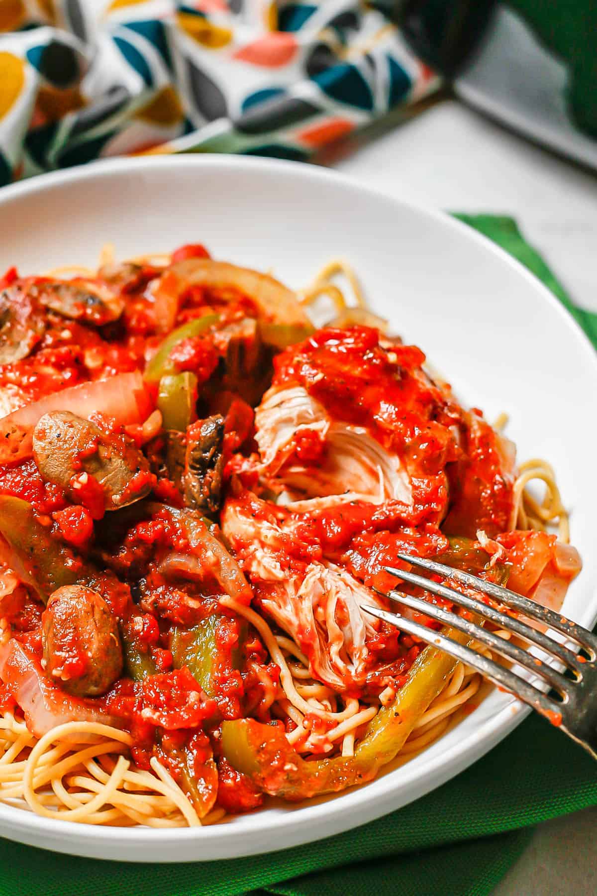 A fork resting on a low white bowl with chicken cacciatore served over spaghetti.