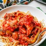 Chicken cacciatore served over spaghetti in a low white bowl with a fork to the side and a text overlay on the photo.