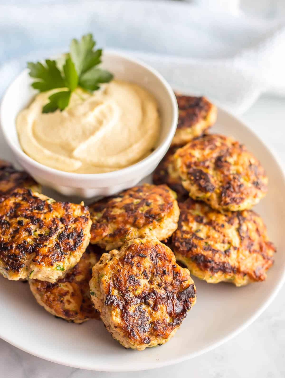 Spicy chicken patties piled on a white plate with a small white bowl of a creamy dipping sauce.