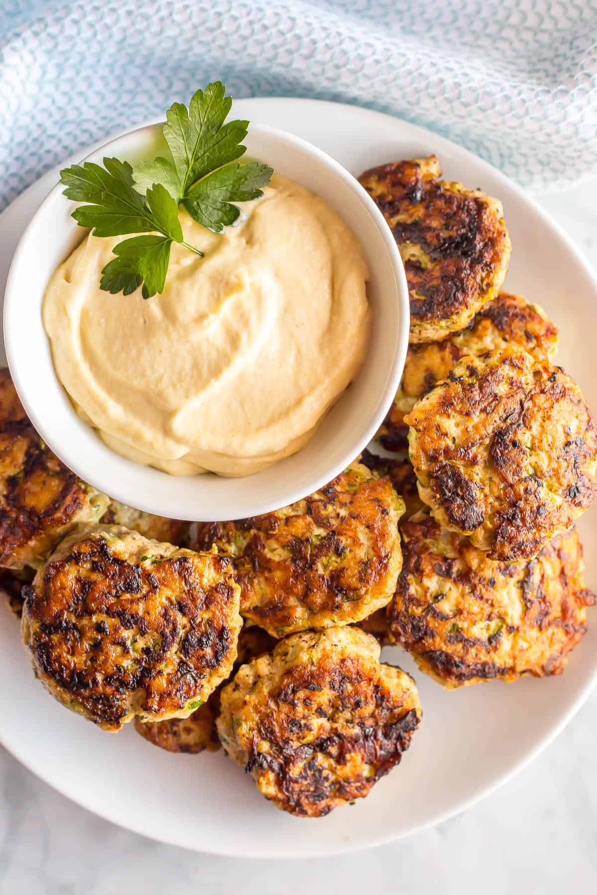 A white plate with spicy chicken patties and a creamy dipping sauce in a bowl to the side.