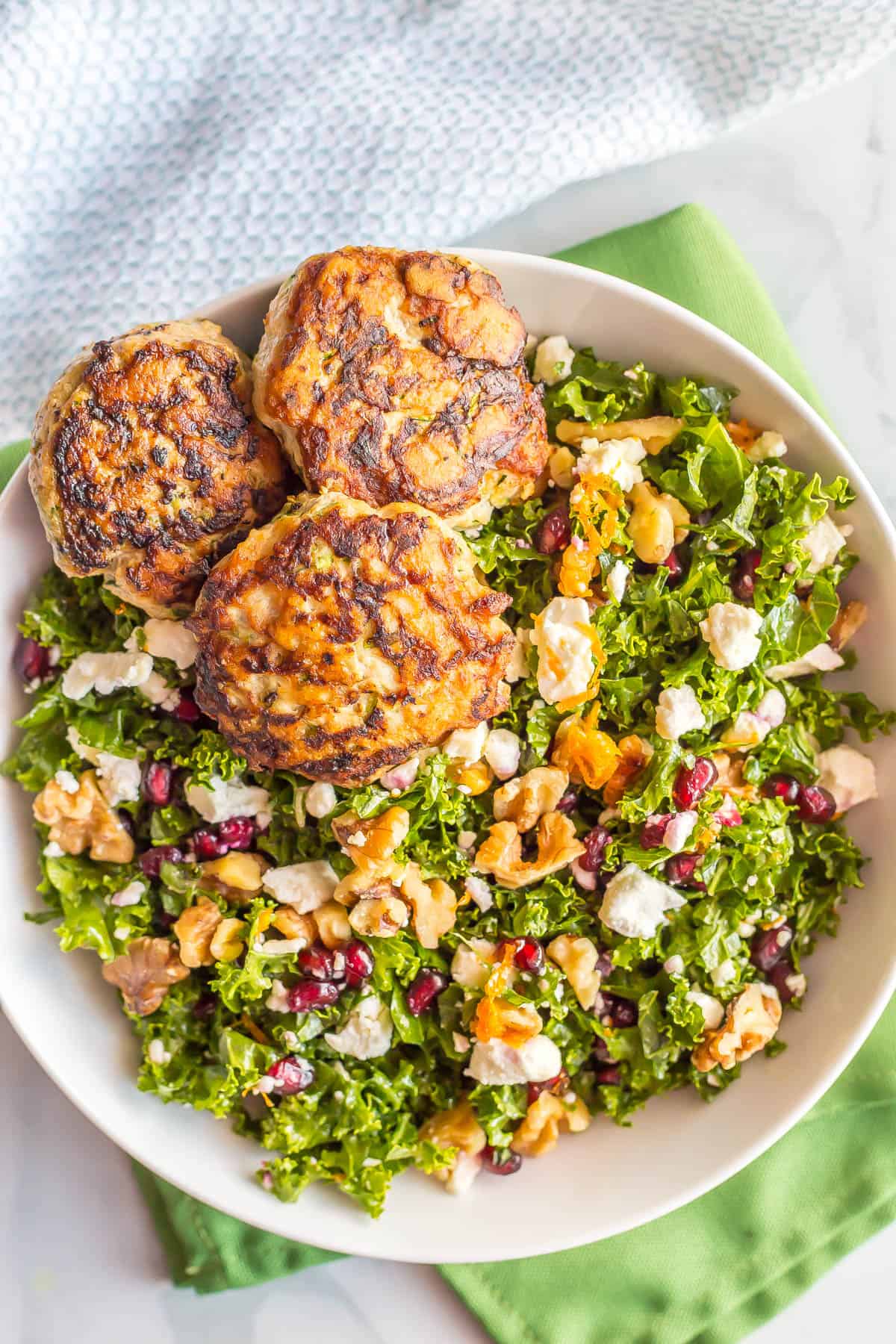 A massaged kale salad with feta, walnuts and three spicy chicken patties on top.