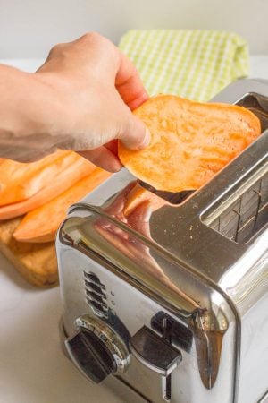 A hand putting a sweet potato slice into a toaster.