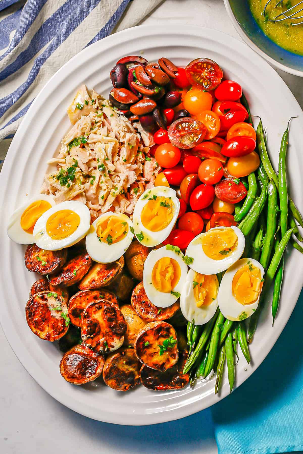 Niçoise salad with potatoes, hard boiled eggs, green beans, tomatoes, tuna and olives arranged on a large white platter.