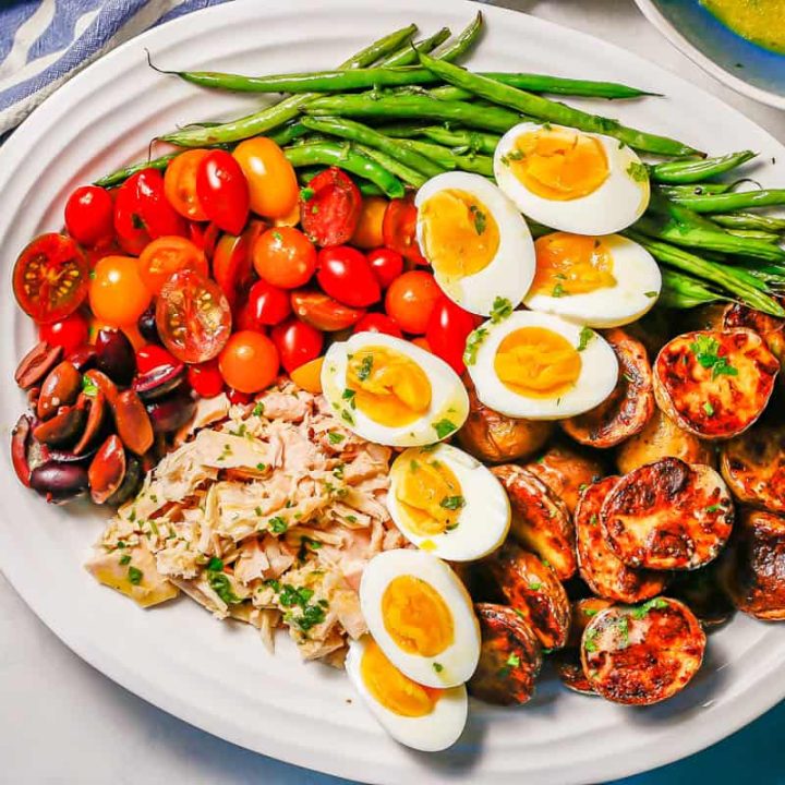 An arranged Niçoise salad on a white platter with colorful napkins nearby.