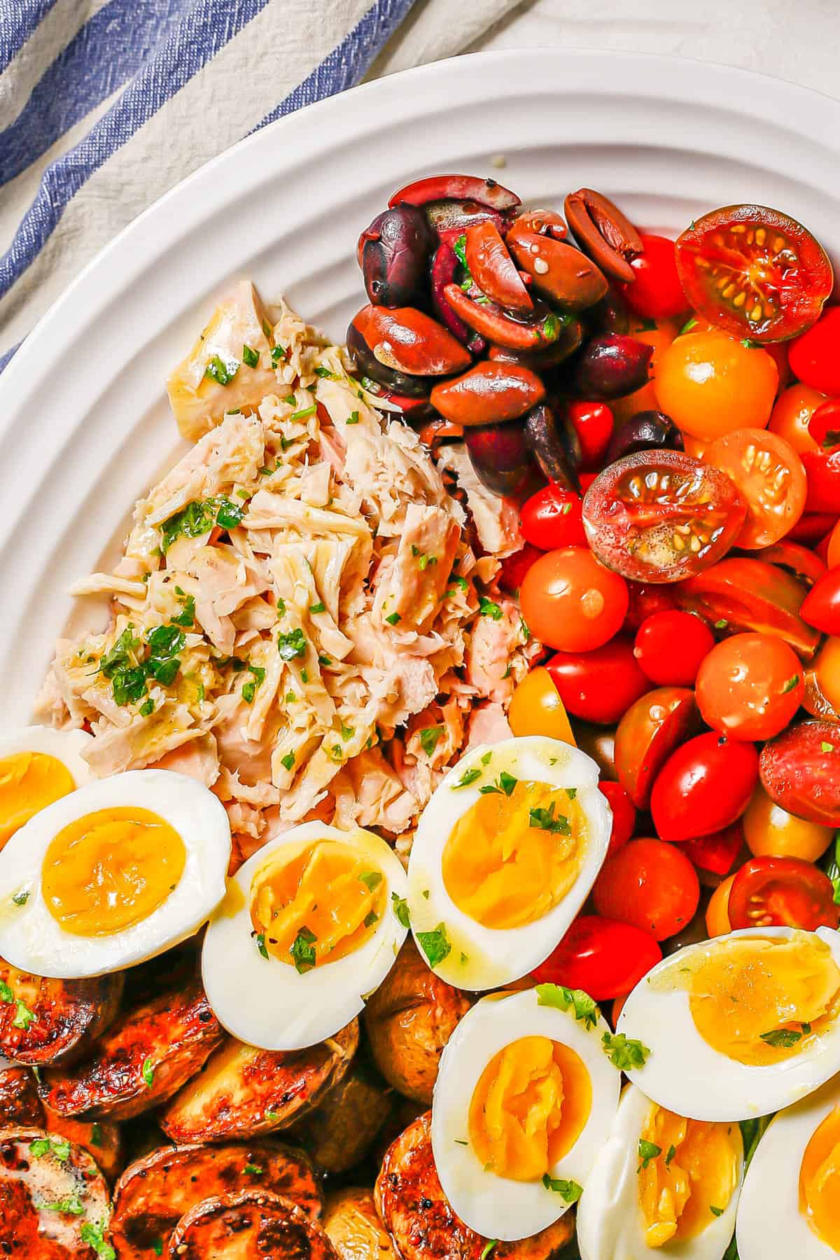 Close up of tuna, olives, tomatoes and hard boiled eggs on a white platter.