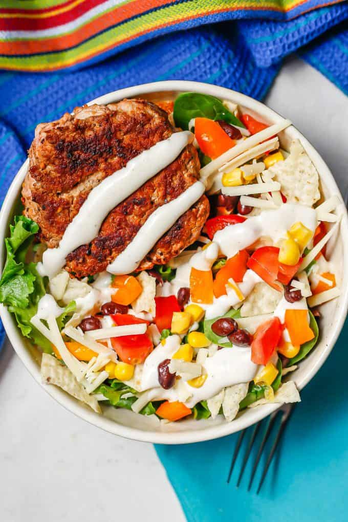 A salad bowl with beans, corn, tomatoes and a turkey burger, drizzled with Ranch.