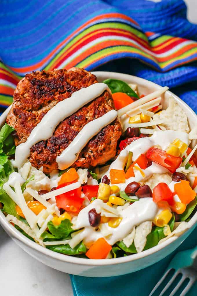 A salad bowl with beans, corn, tomatoes, peppers, cheese and a turkey burger, drizzled with Ranch.
