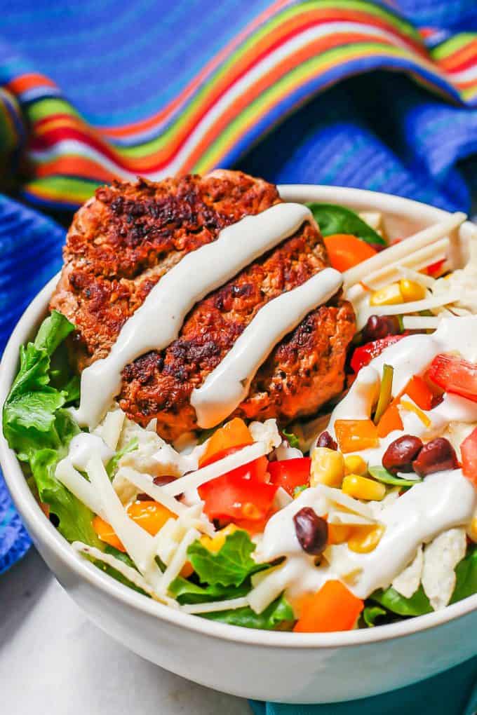 Close up of a mixed greens salad bowl with beans, corn, tomatoes, peppers, cheese and a turkey burger, drizzled with Ranch.