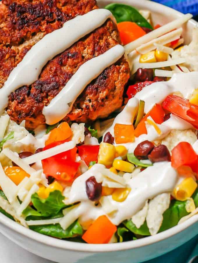 A colorful turkey burger salad bowl drizzled with Ranch dressing.