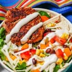 A salad bowl with beans, corn, tomatoes, peppers, cheese and a turkey burger, drizzled with Ranch with a text box on the photo.