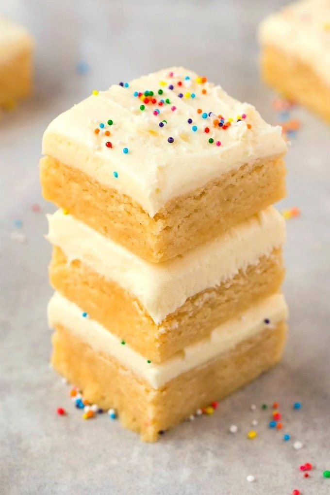 A stack of three healthy no bake sugar cookie bars topped with frosting and sprinkles.