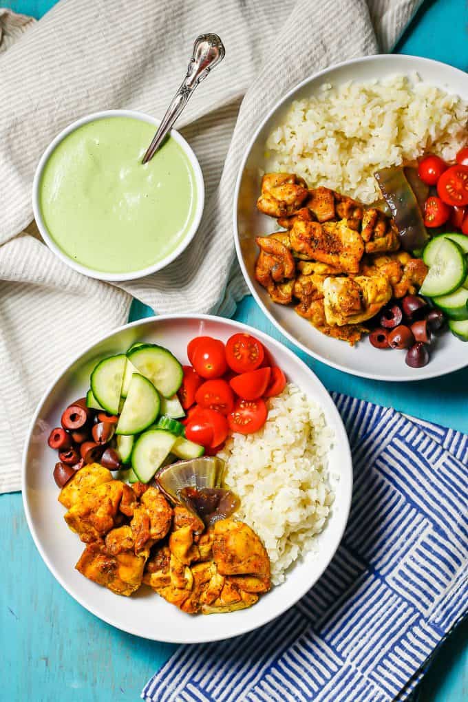 Assembled cauliflower rice bowls with chicken and veggies with a bowl of tahini herb dressing nearby.