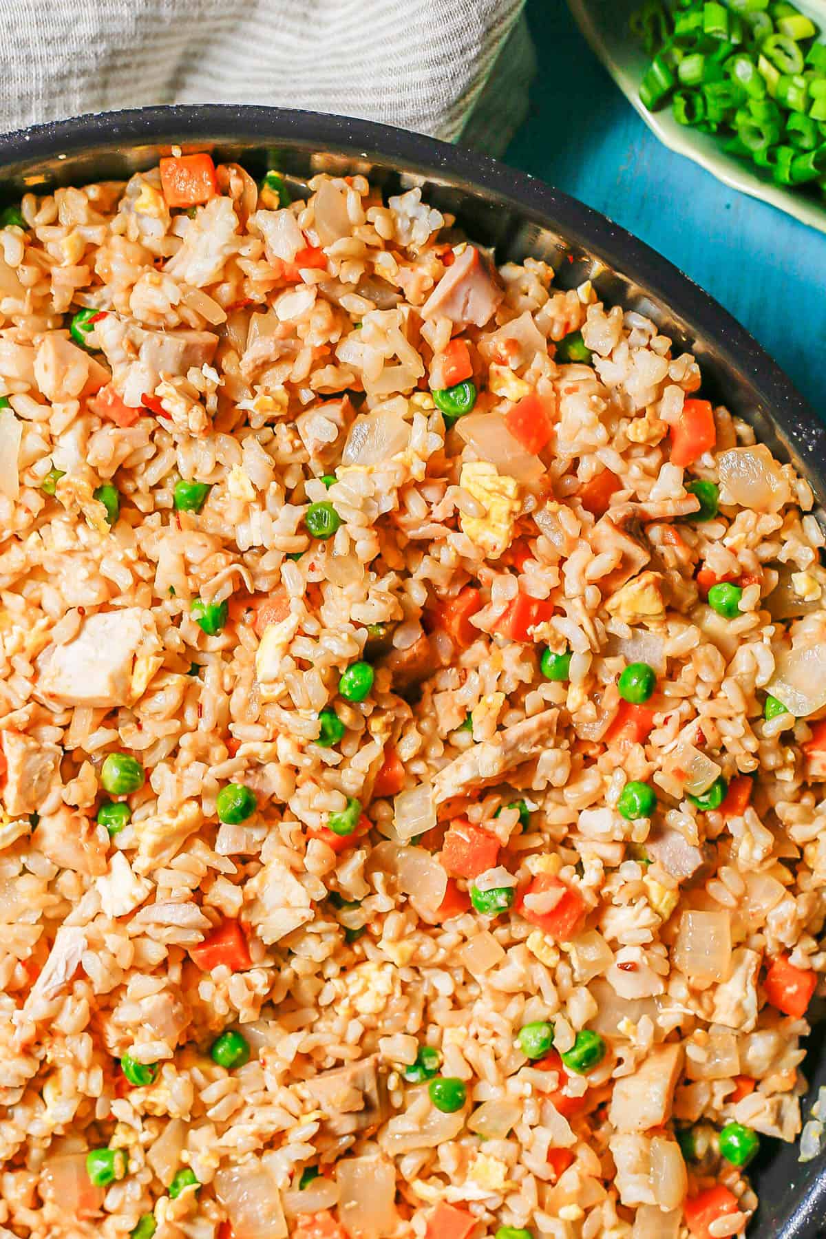 Close up of chicken fried rice with peas and carrots in a large dark skillet.