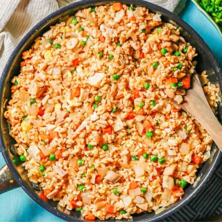 Fried rice with chicken and veggies in a large skillet with a wooden spoon resting in it.