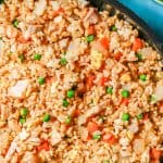 Close up of chicken fried rice with peas and carrots in a large dark skillet with a text overlay on the photo.