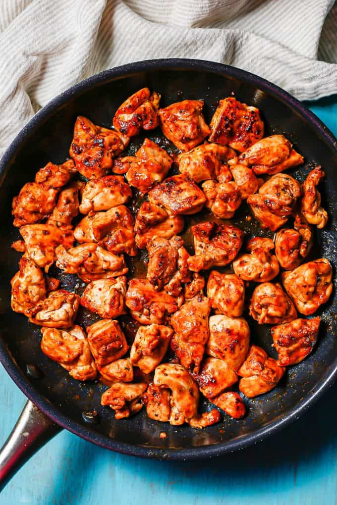 Cubed chunks of paprika seasoned chicken thighs cooking in a large dark skillet.