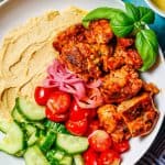Close up of paprika chicken and hummus bowls with fresh veggies in a white bowl with a text overlay on the photo.