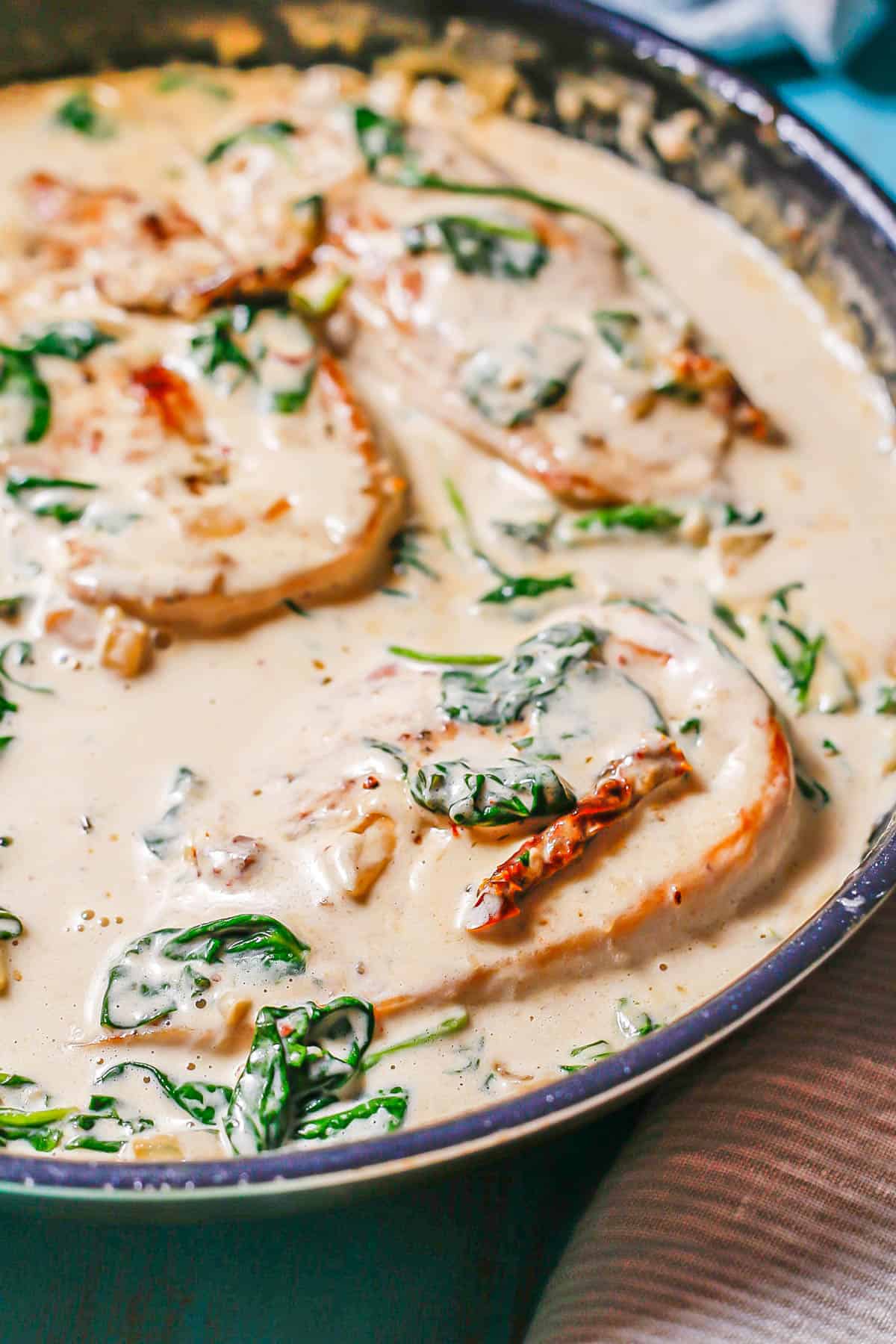 Close up of a chicken breast in a creamy sauce with spinach and sun dried tomatoes in a large dark skillet.
