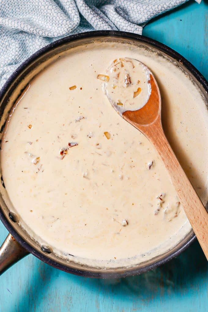 A creamy sauce in a large dark skillet with a wooden spoon resting in it.