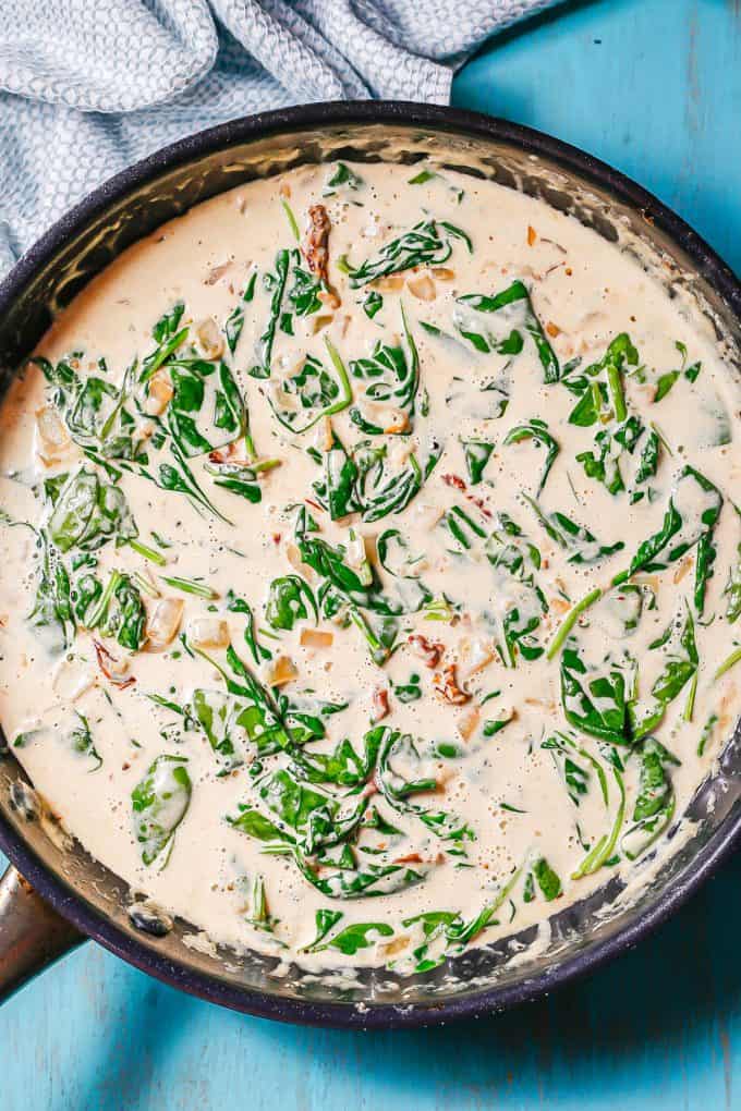 A creamy sauce with spinach and sun dried tomatoes in a large dark skillet.