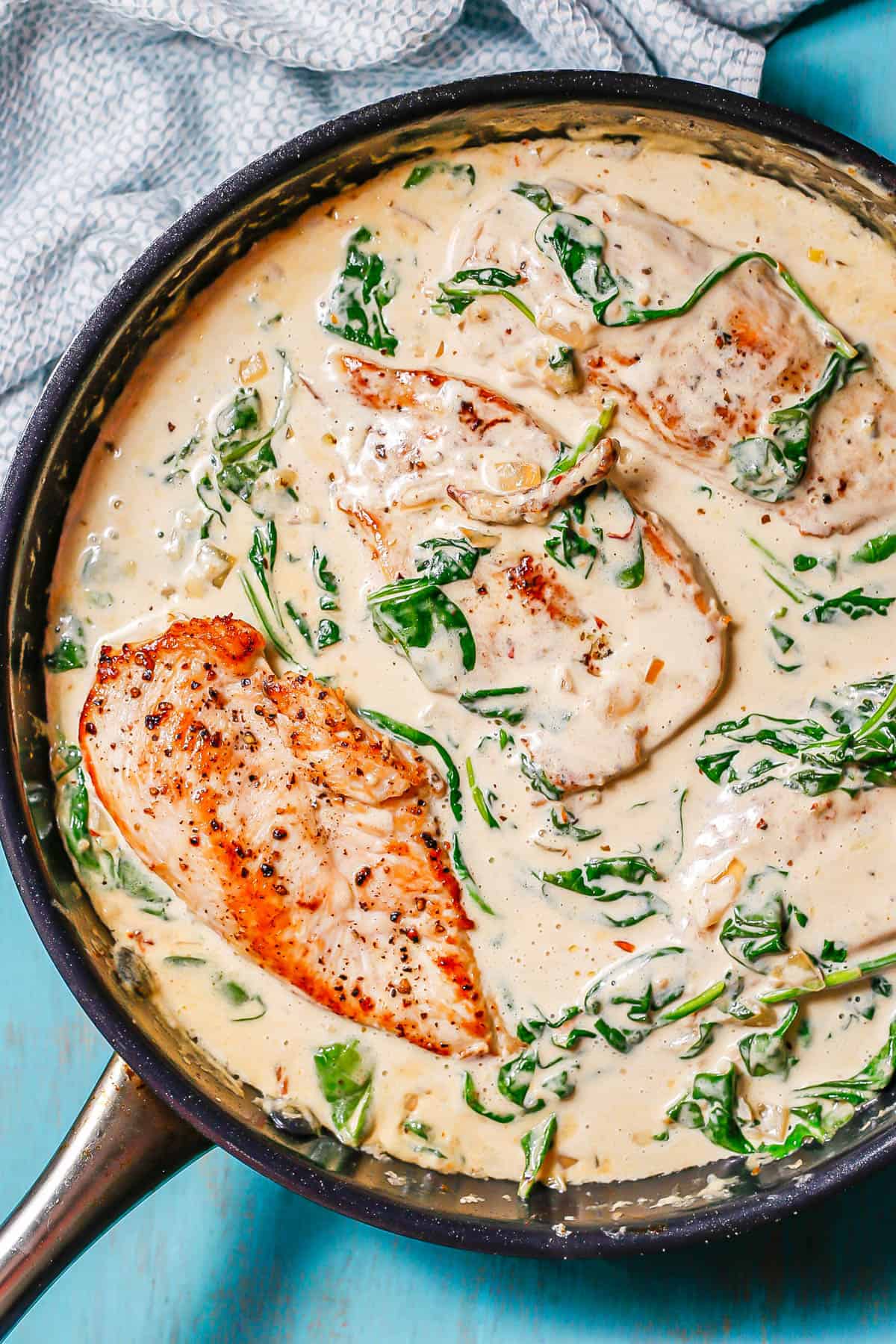 Tuscan chicken with spinach and sun dried tomatoes in a creamy white sauce in a skillet.