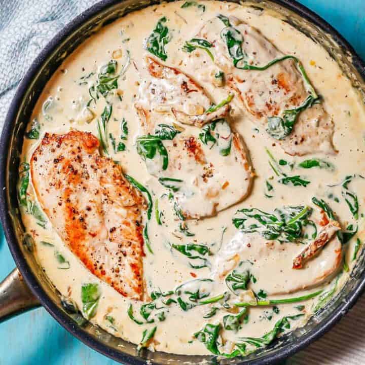 A large skillet with creamy Tuscan chicken cutlets in a creamy sauce with spinach and sun dried tomatoes.
