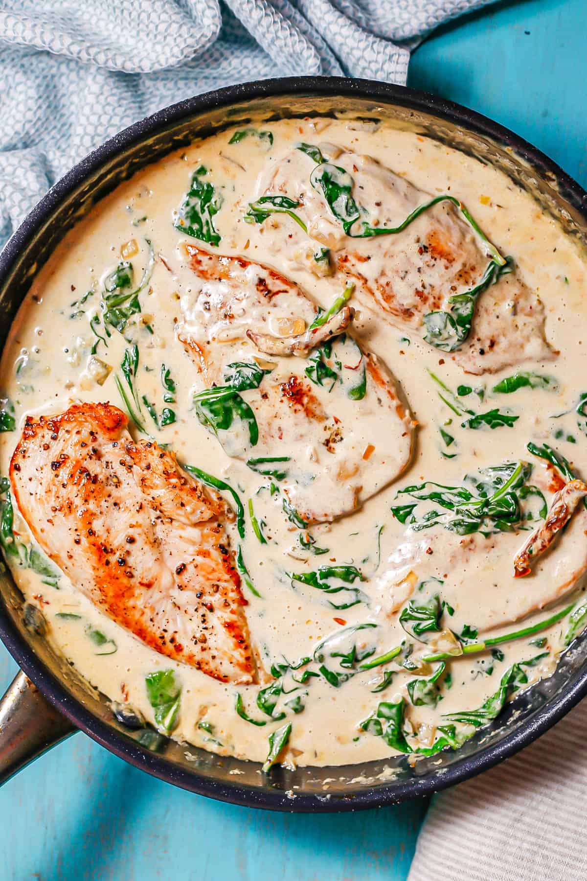 A large dark skillet with creamy Tuscan chicken cutlets in a creamy sauce with spinach and sun dried tomatoes.