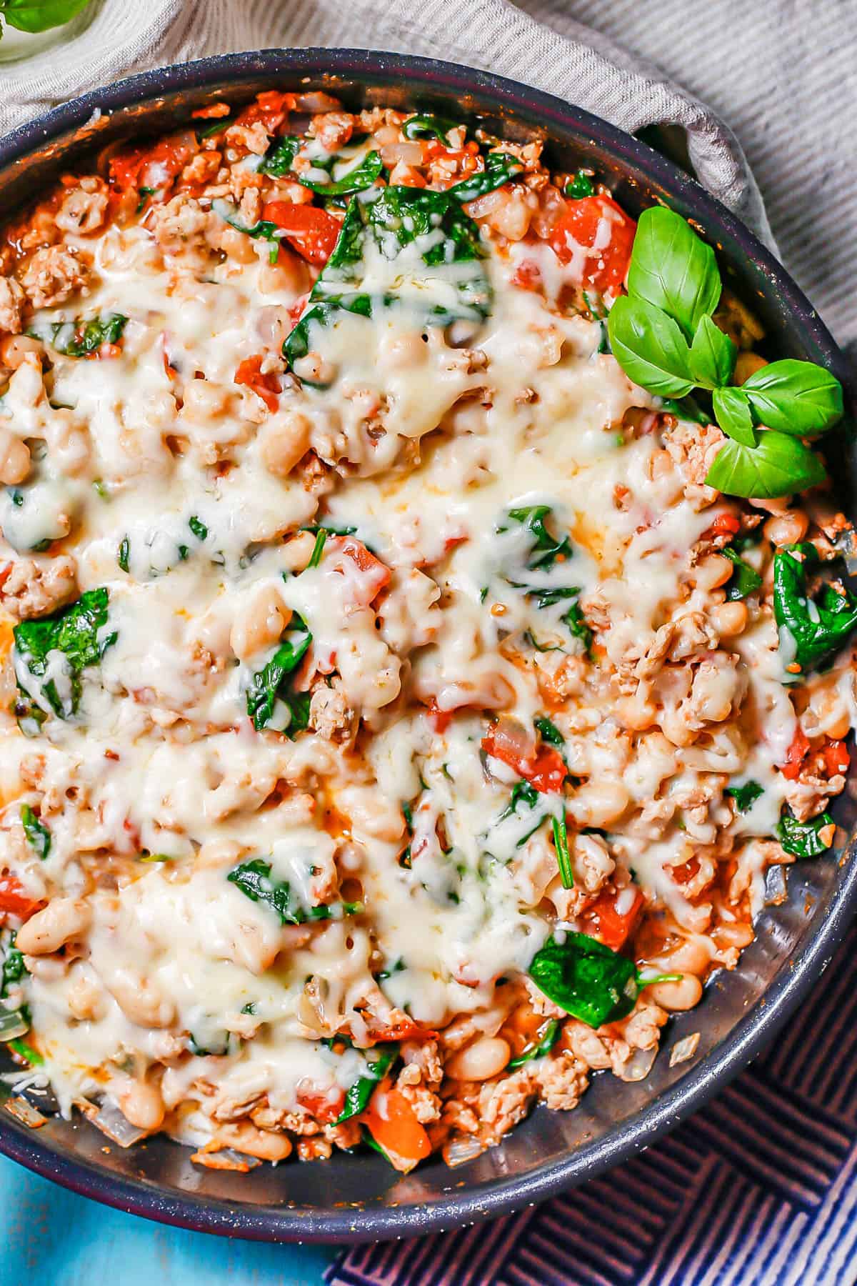 A large dark skillet with a ground chicken and veggie mixture topped with melted mozzarella cheese.