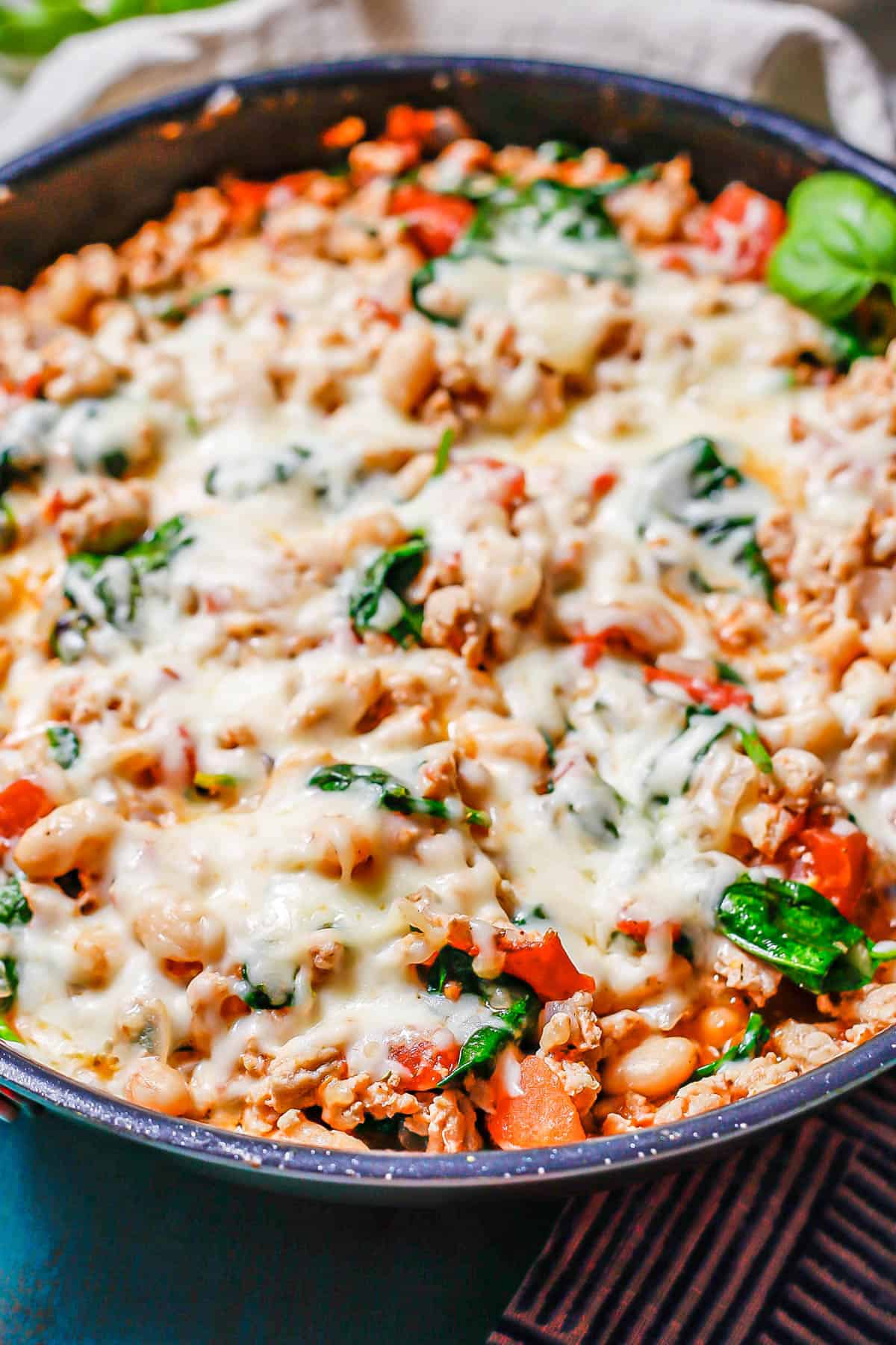 Cheesy ground chicken and white beans with tomatoes and spinach in a large dark pan.