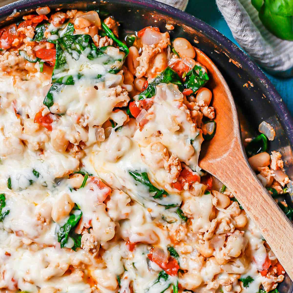 A wooden spoon scooping up a chicken, bean and veggie mixture for a large pan.