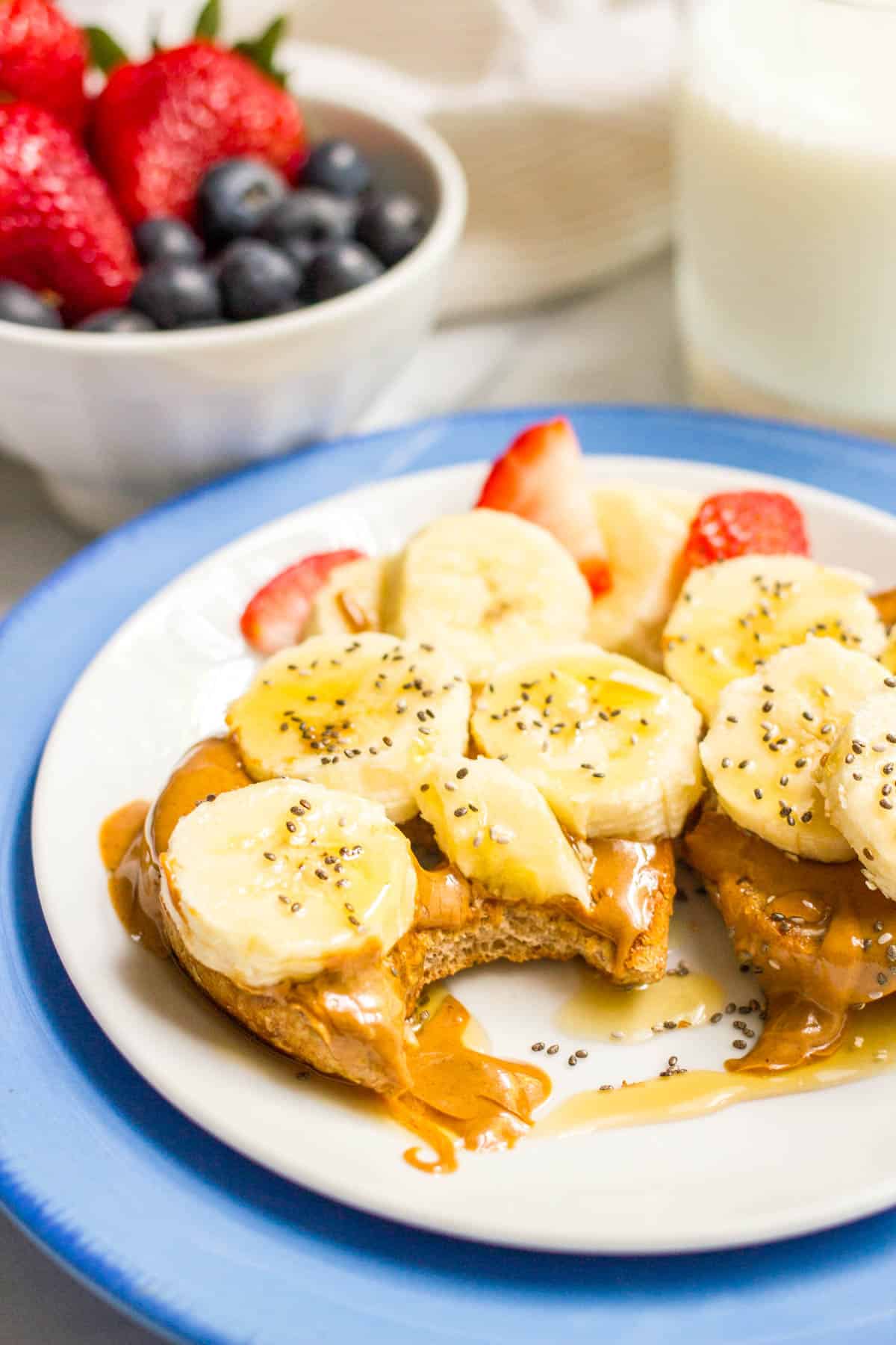 A bite taken out of a bagel topped with peanut butter, sliced bananas, chia seeds and a drizzle of honey.