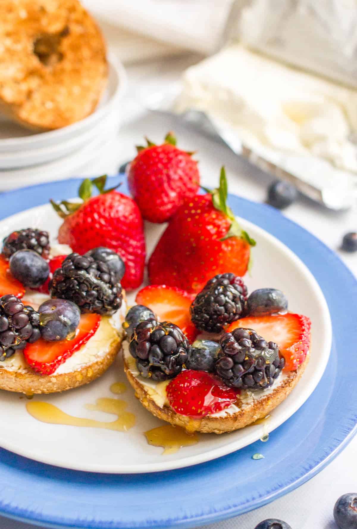 A bagel topped with cream cheese, fresh berries and a drizzle of honey.