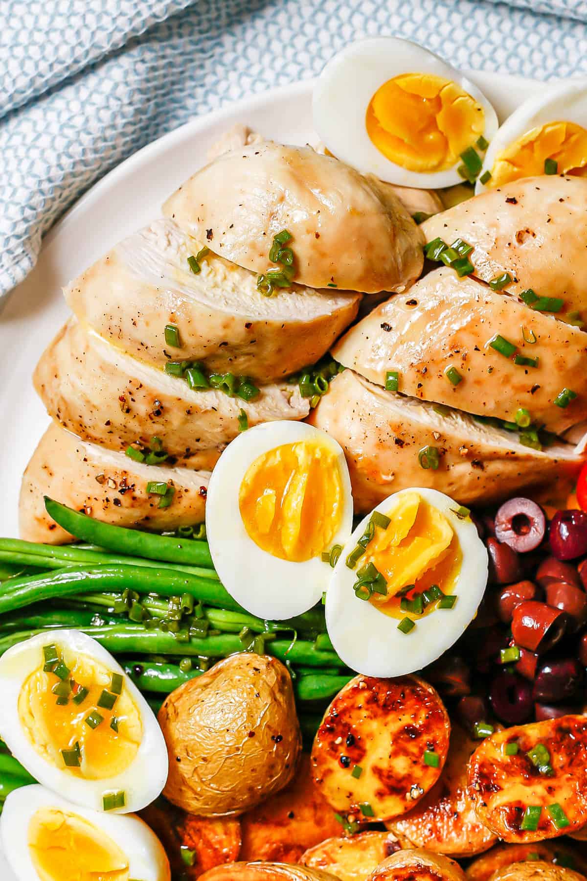 Close up of sliced roasted chicken breasts on a Niçoise salad platter.