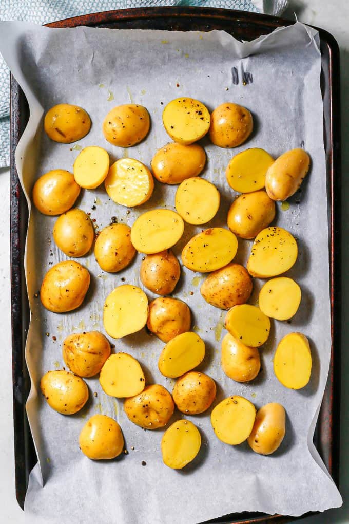 Halved gold potatoes on a parchment paper lined baking sheet before being cooked.