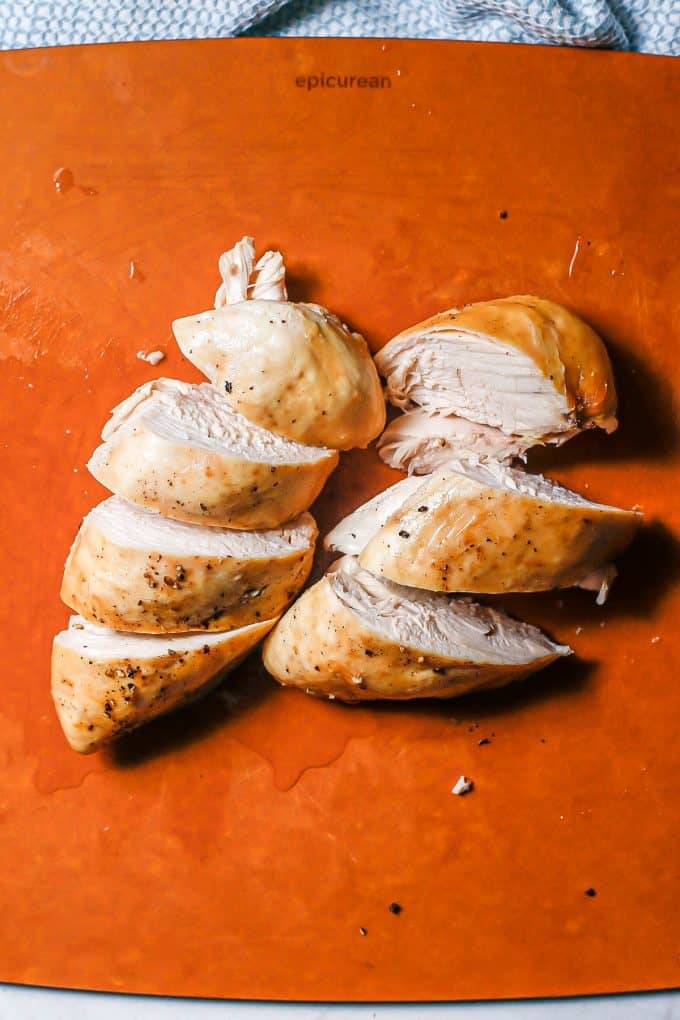 Roasted chicken breasts on a cutting board cut into thick slices.