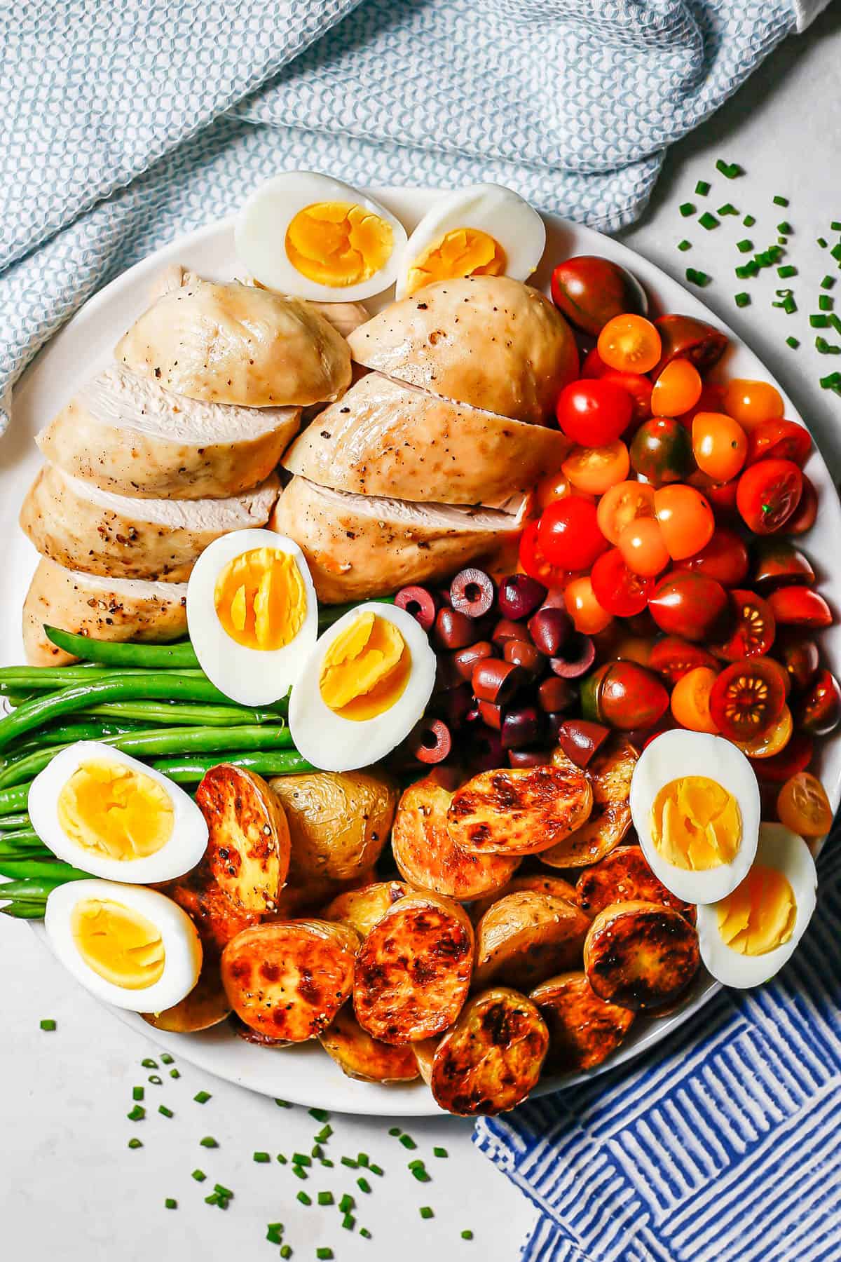 A large white platter with roast chicken Niçoise salad before being drizzled with dressing.