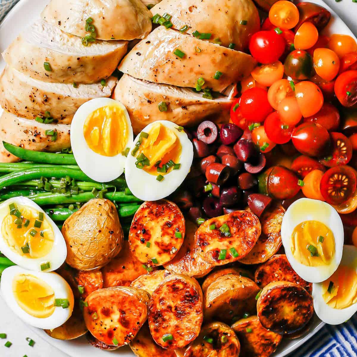 Close up of roast chicken Niçoise salad with tomatoes, olives, hard boiled eggs, roasted potatoes and haricot verts.