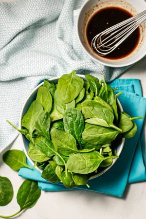 A bowl full of fresh baby spinach sitting on teal napkins with a bowl of balsamic vinaigrette nearby.