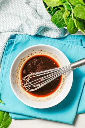 A bowl of balsamic vinaigrette with a whisk resting in it set on teal napkins.