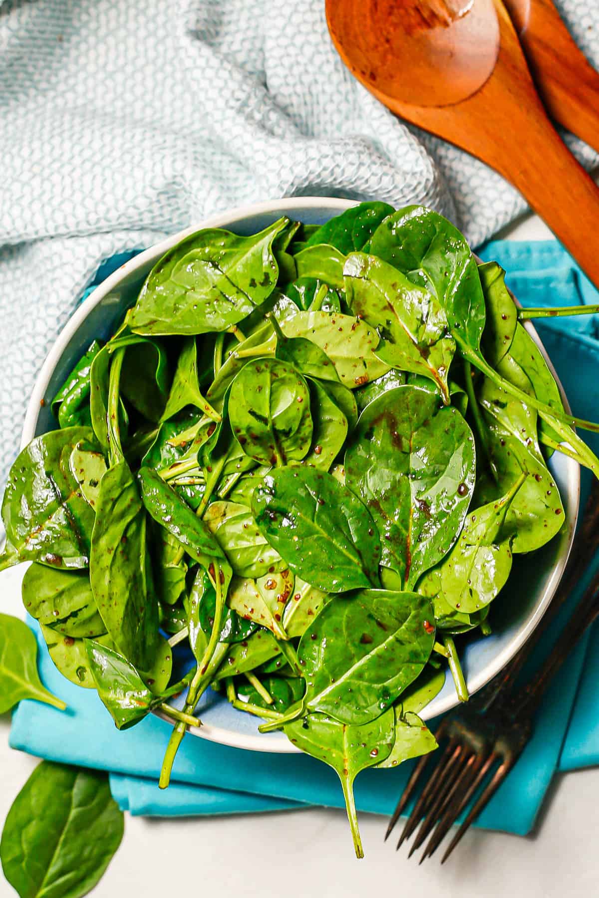 Baby spinach dressed with balsamic vinaigrette in a large blue and white bowl with wooden salad utensils to the side.