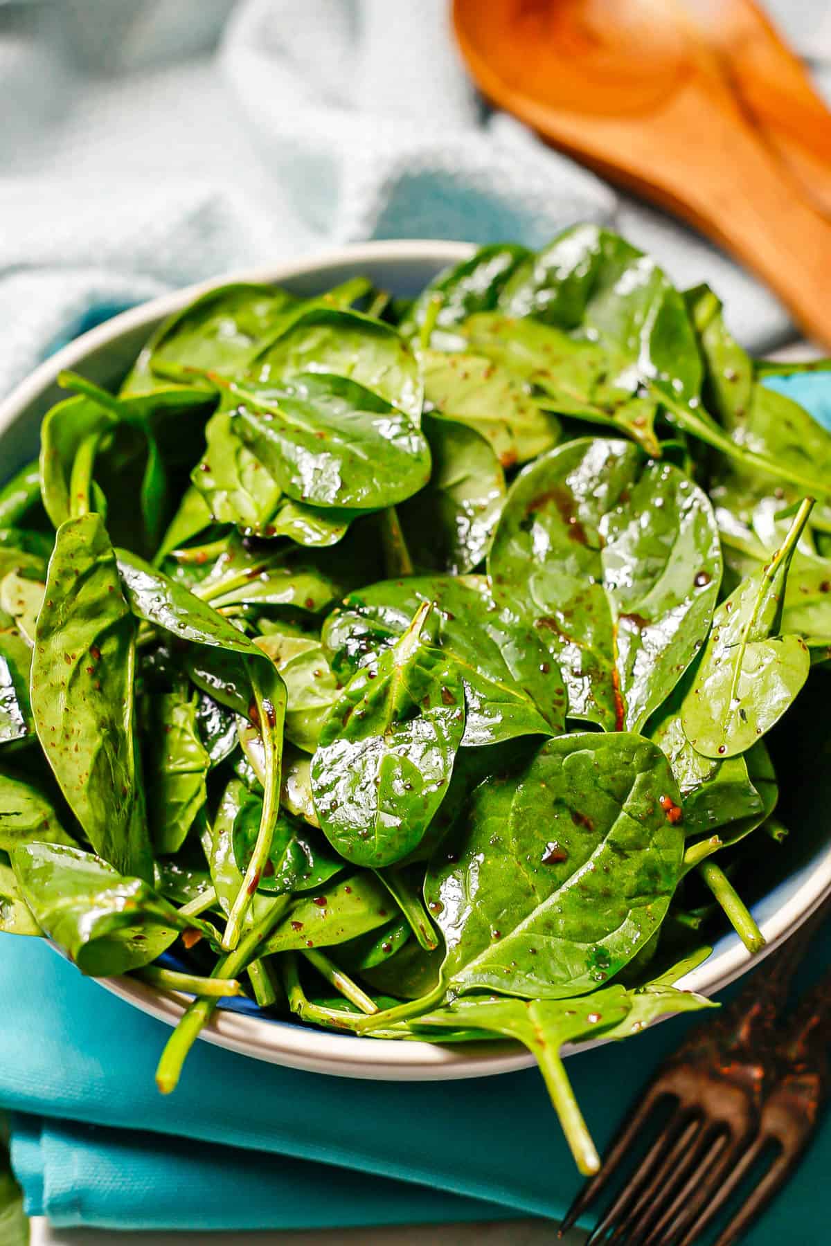 Close up of a spinach salad with balsamic vinaigrette dressing in a large serving bowl.
