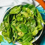Baby spinach dressed with balsamic vinaigrette in a large blue and white bowl with wooden salad utensils to the side and a text overlay on the photo.