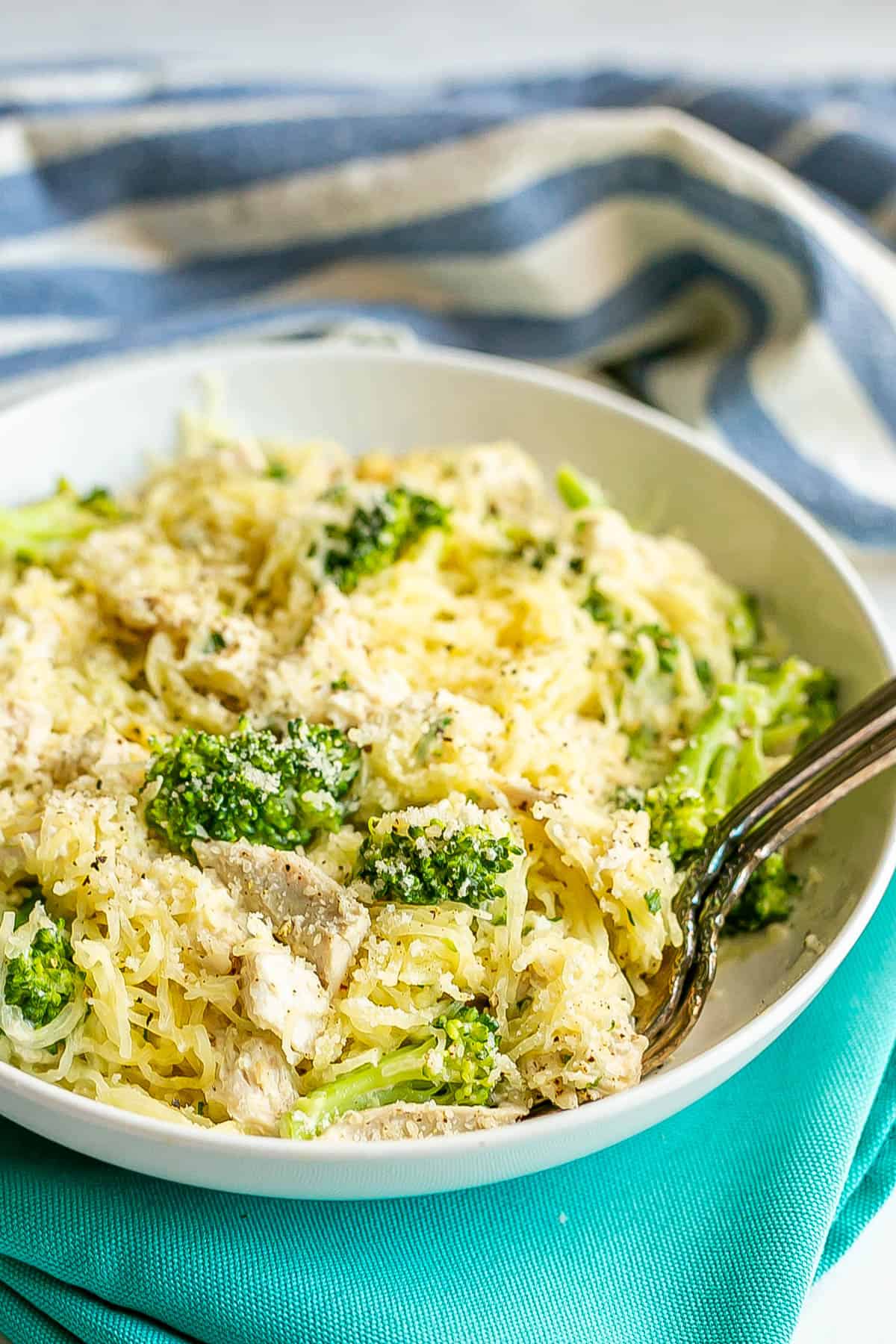 Spaghetti squash with chicken and broccoli topped with Parmesan cheese served in a low white bowl with two forks resting in it.